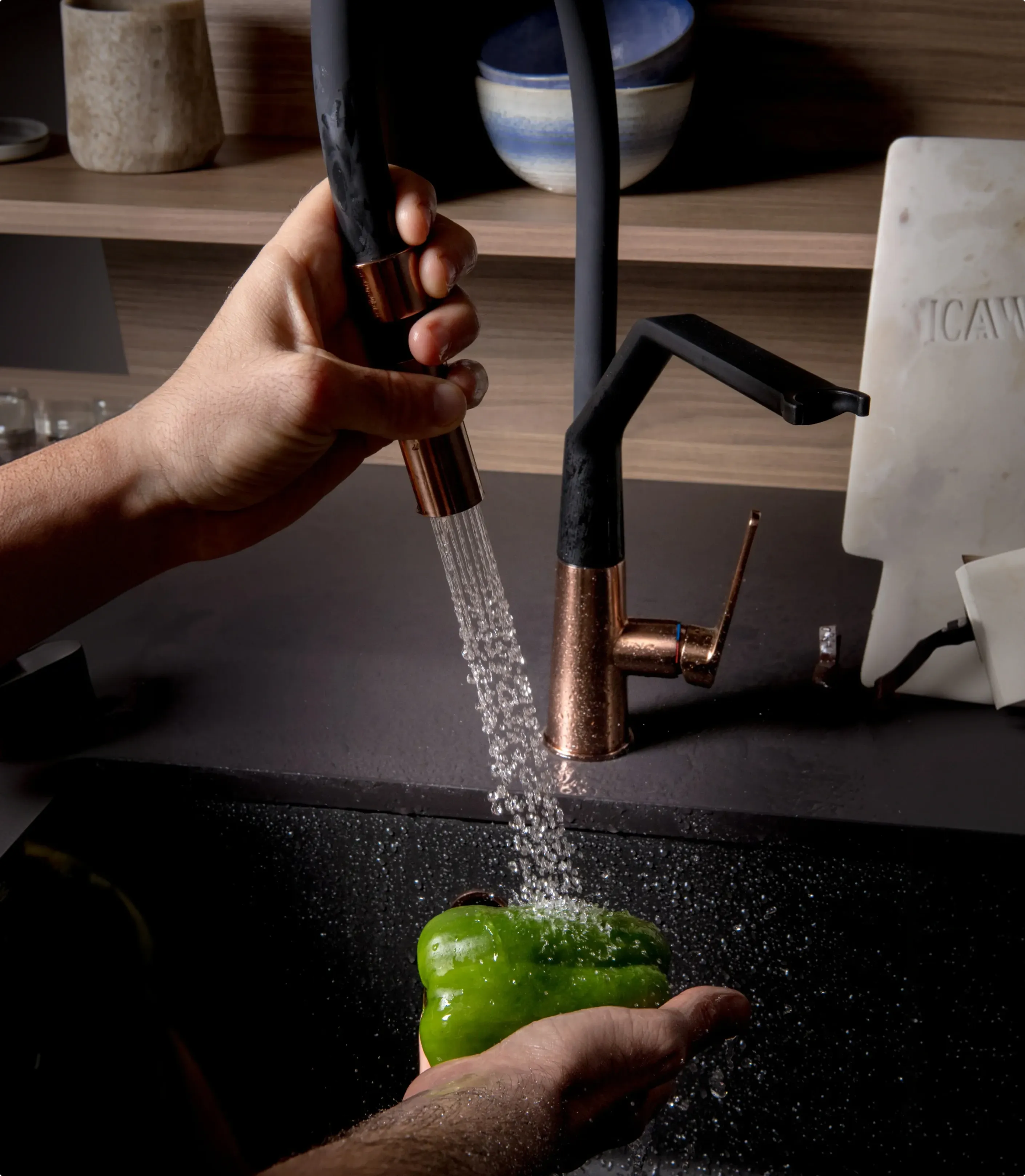 Persona lavando un pimiento verde con el grifo etna semipro cobre y negro de ICOBEN
